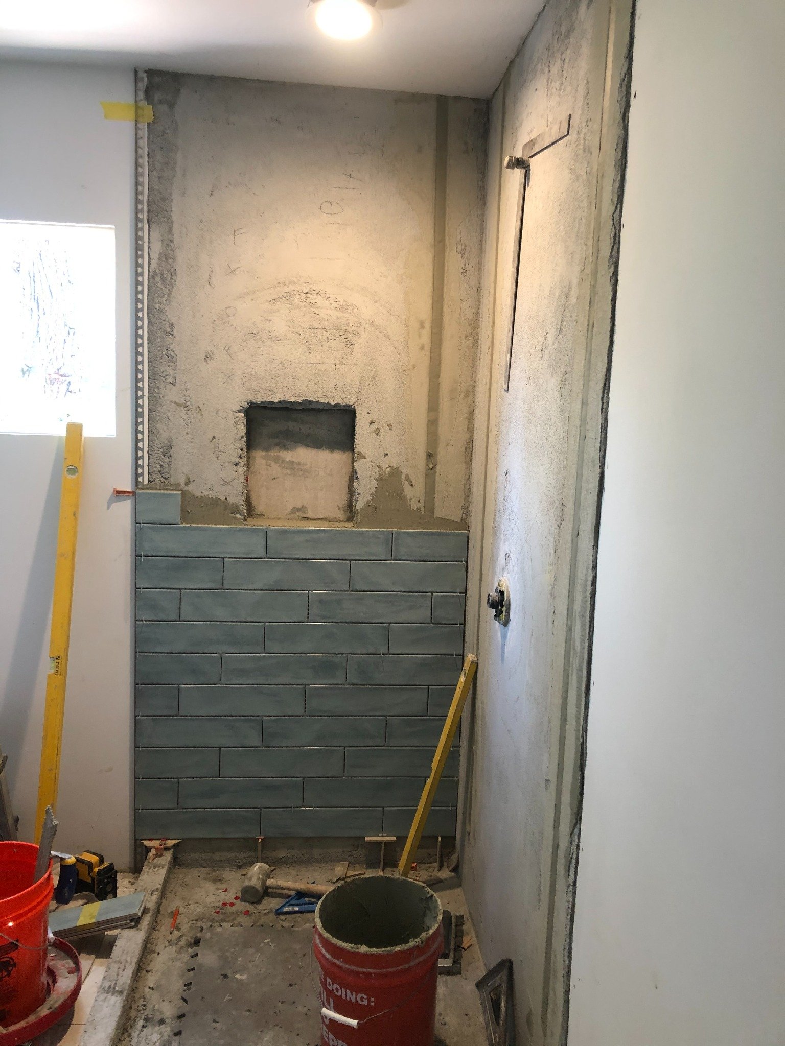 Blue-gray shower tile during installation with unfinished walls and tools