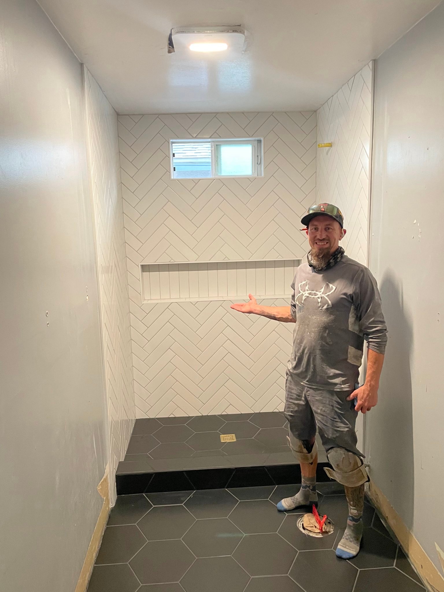 Completed white herringbone custom shower tile with dark hexagonal floor