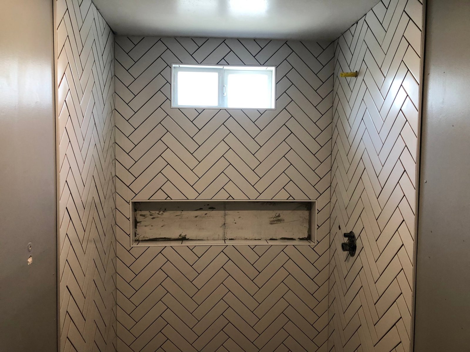 White herringbone shower tile during installation with unfinished niche