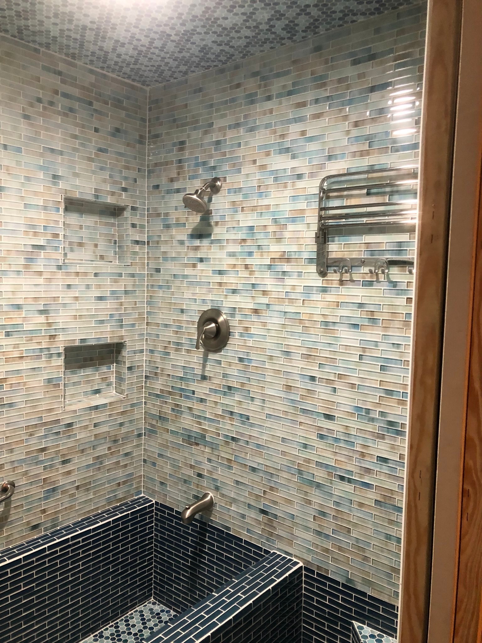 Completed custom mosaic shower with glass wall tile, dark lower tile, niches and seating